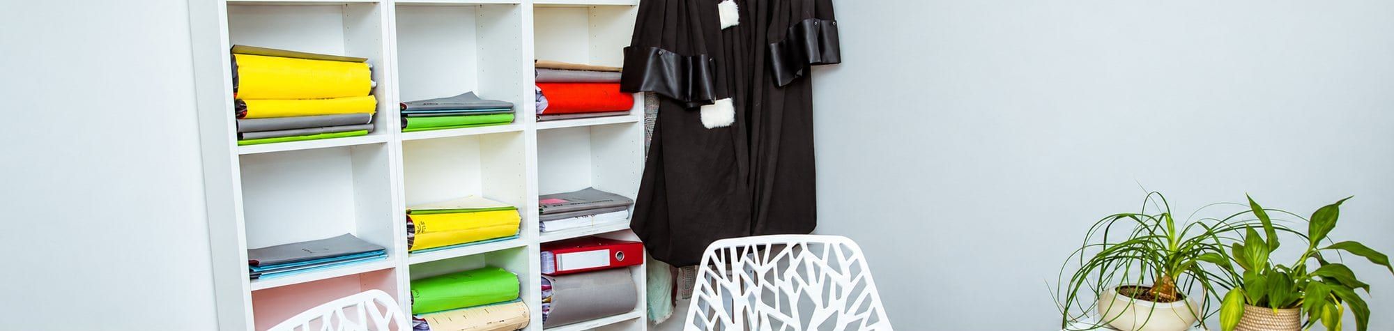 Bureau d’avocat avec robe noire, étagère de dossiers colorés et chaises blanches.