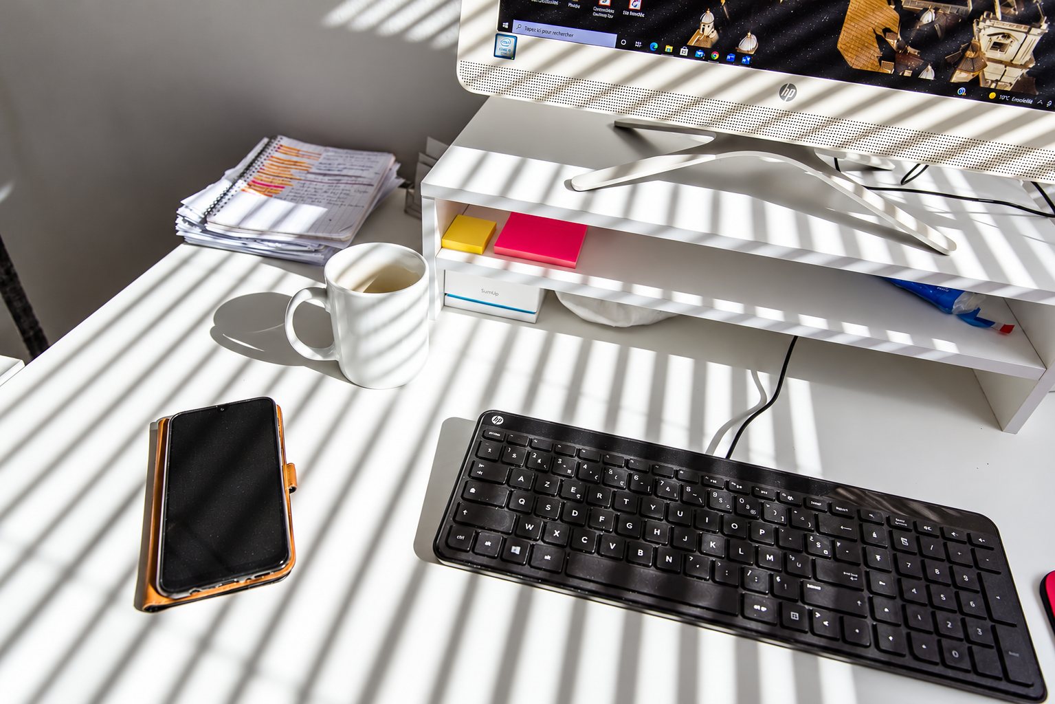 Bureau blanc sous la lumière du soleil, avec clavier, tasse et téléphone.