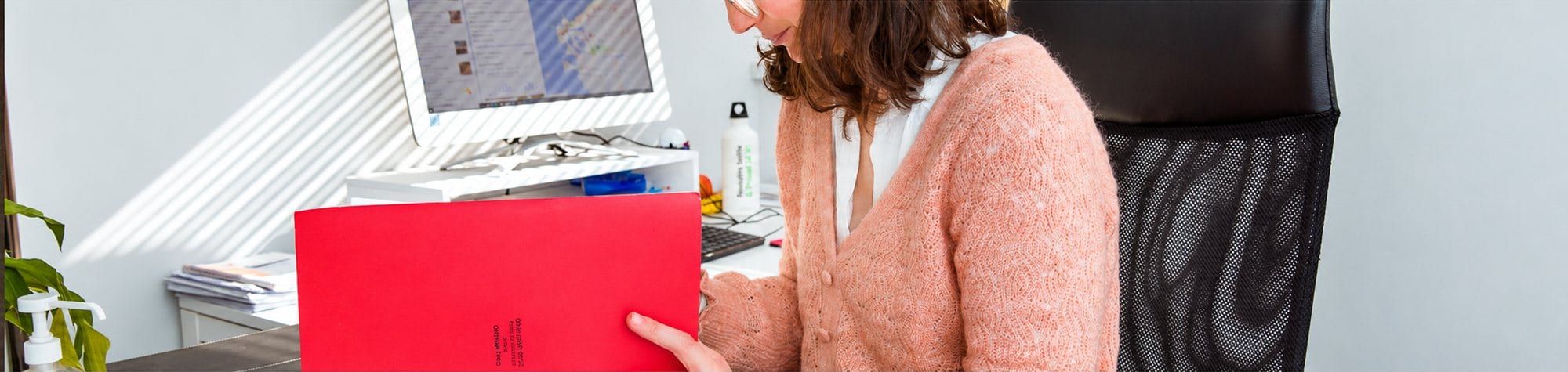 Femme consultant un dossier rouge au bureau.